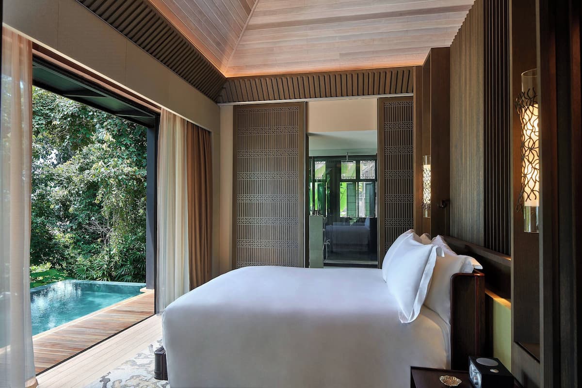 A bedroom with a large bed, a wooden deck, and a view of a swimming pool.
