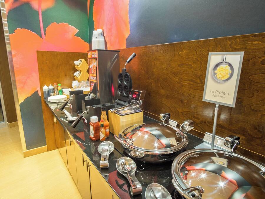 A buffet setup with a variety of food containers, condiment bottles, and a waffle maker.