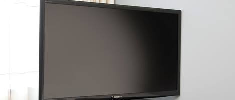 Un televisor de pantalla plana sobre un soporte de madera, frente a una pared de color claro.