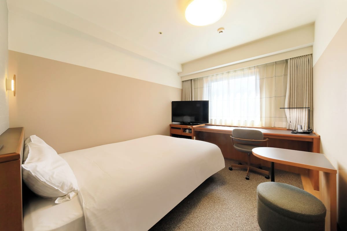 A hotel room with a bed, a desk, a chair, a television, and a window with curtains.