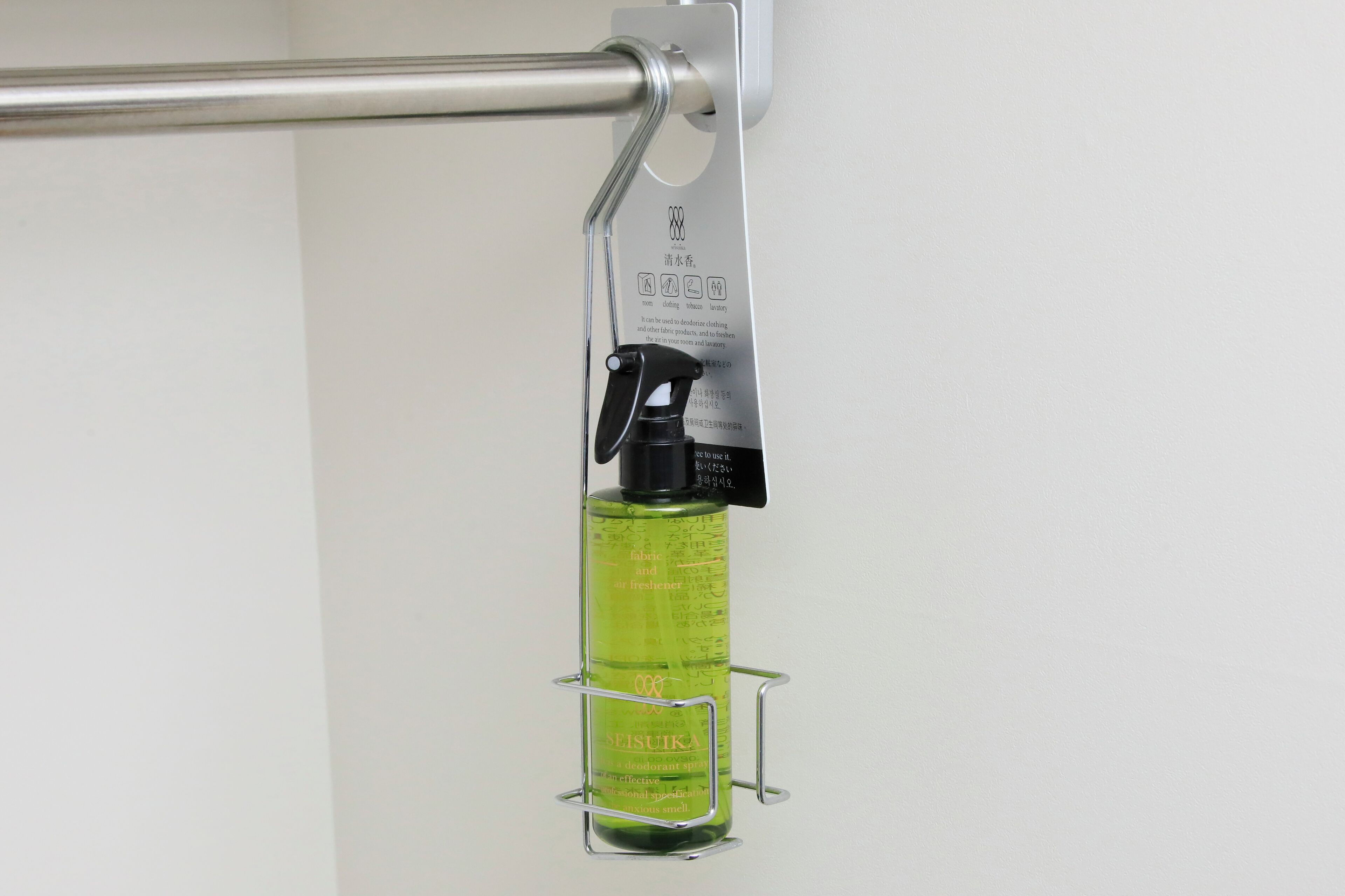 A green bottle of Seisuiya deodorant hanging on a metal rack attached to a wall.