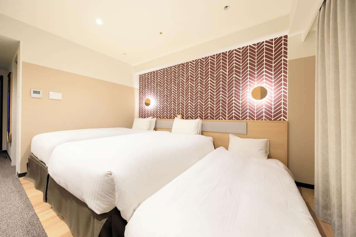 A hotel room with two beds, a patterned wall, and a ceiling light.