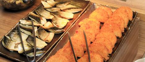 Een buffet met diverse gerechten, waaronder gebakken vis en andere bereide maaltijden.