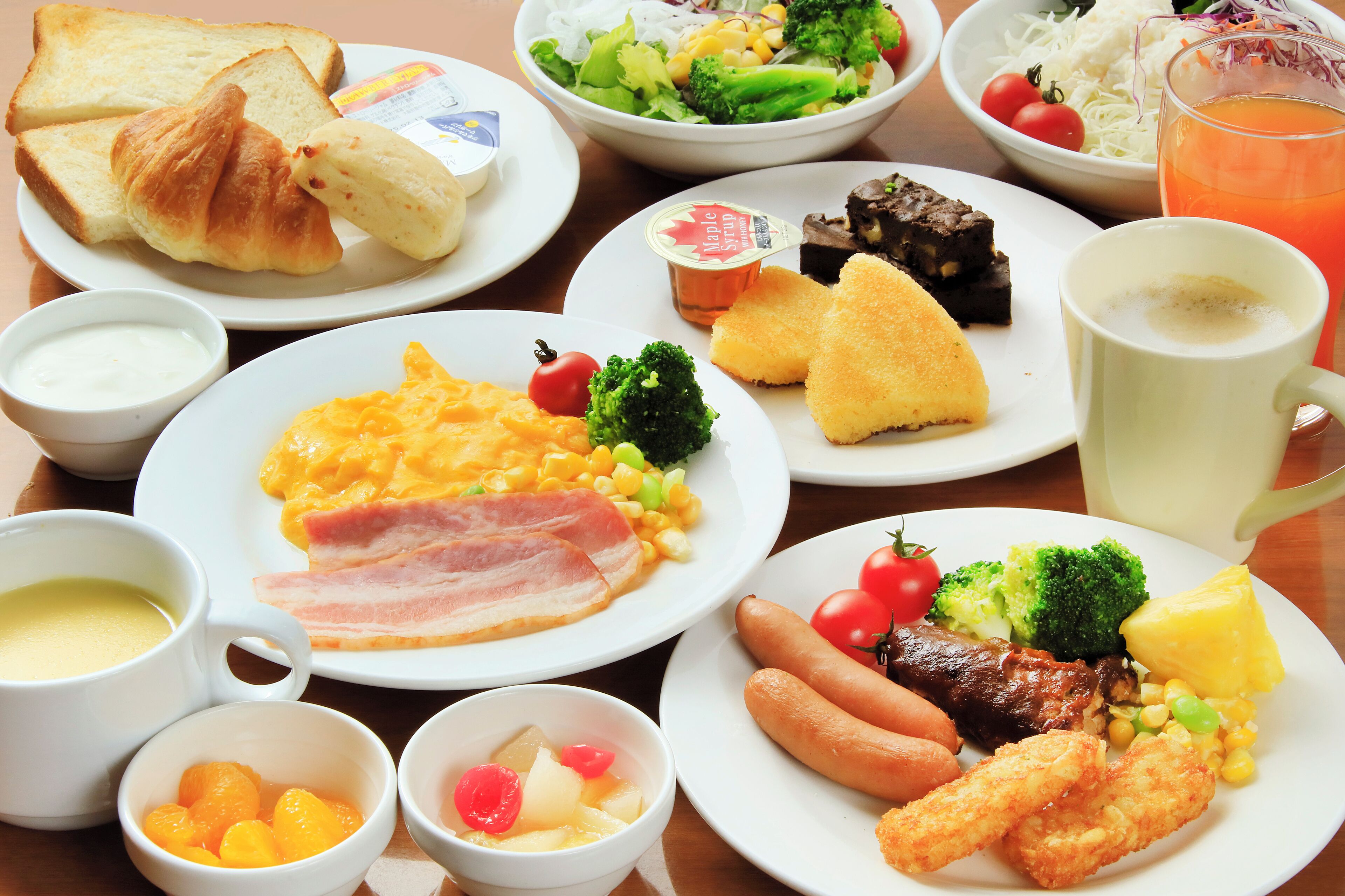 Une table garnie de divers aliments pour le petit-déjeuner, notamment des toasts, des œufs brouillés, du bacon, des saucisses et un verre de jus d’orange.