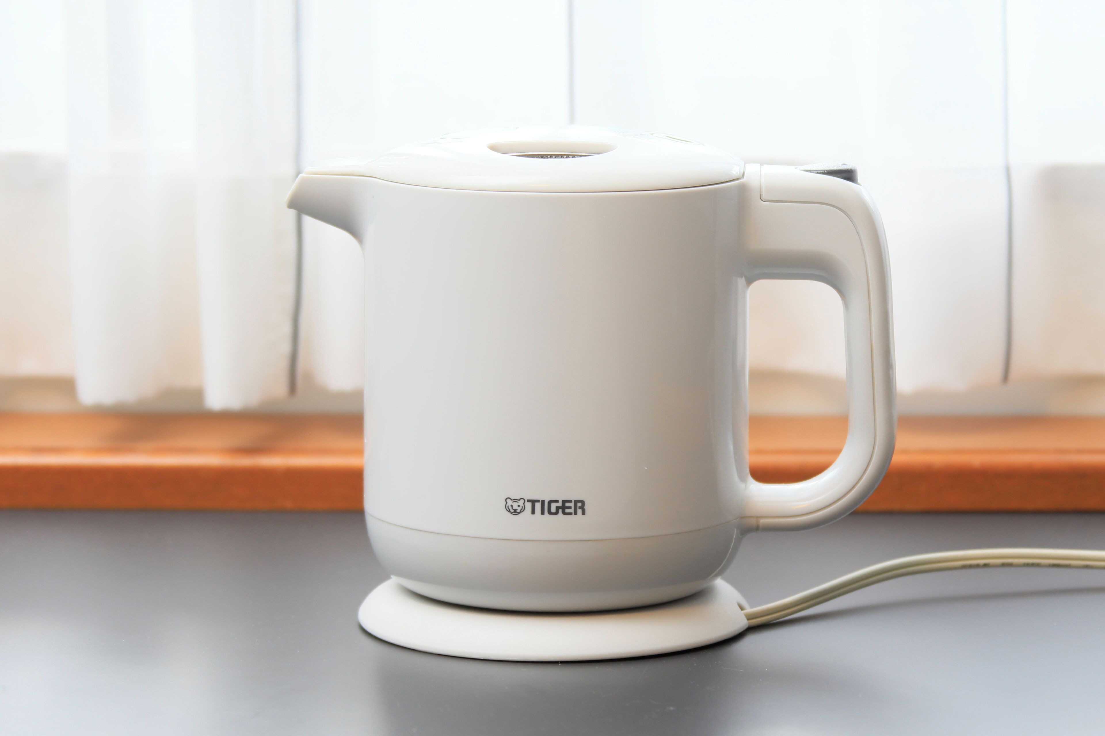 A white electric kettle with a handle and cord on a flat surface.