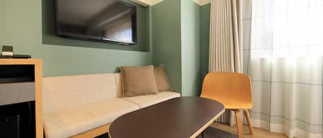 A modern living room with a flat-screen TV mounted on the wall, a sofa, a wooden chair, and a coffee table.