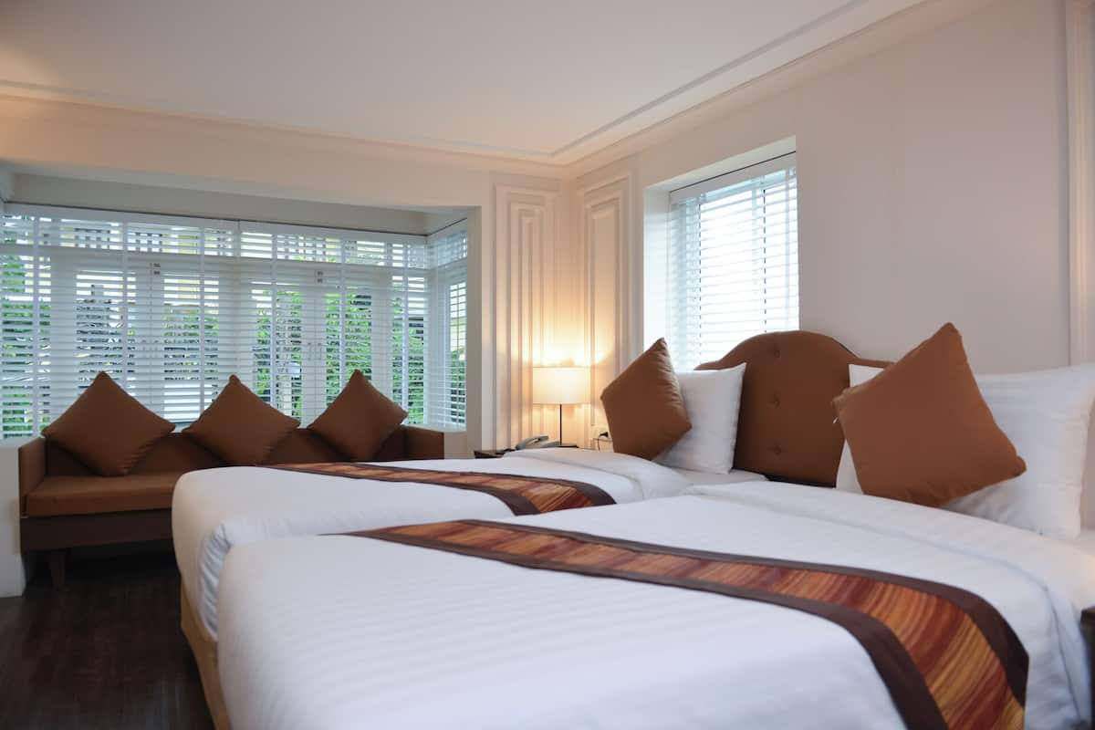 A hotel room with two beds, a sofa, and a window with blinds.