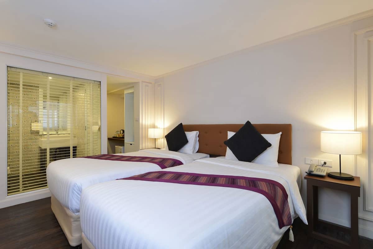 A hotel room with two beds, a bedside table with a lamp, a phone, and a mirror.