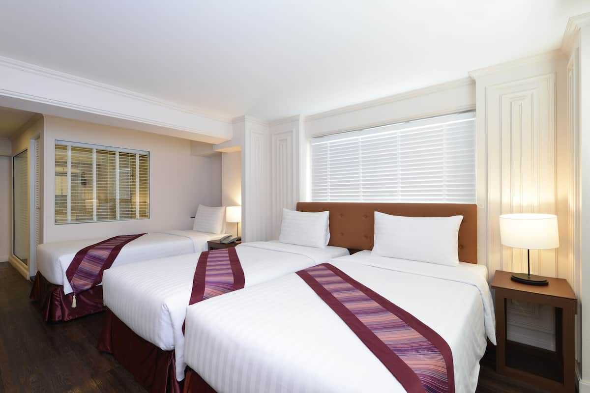 A hotel room with two beds, a nightstand with a lamp, and a window with blinds.