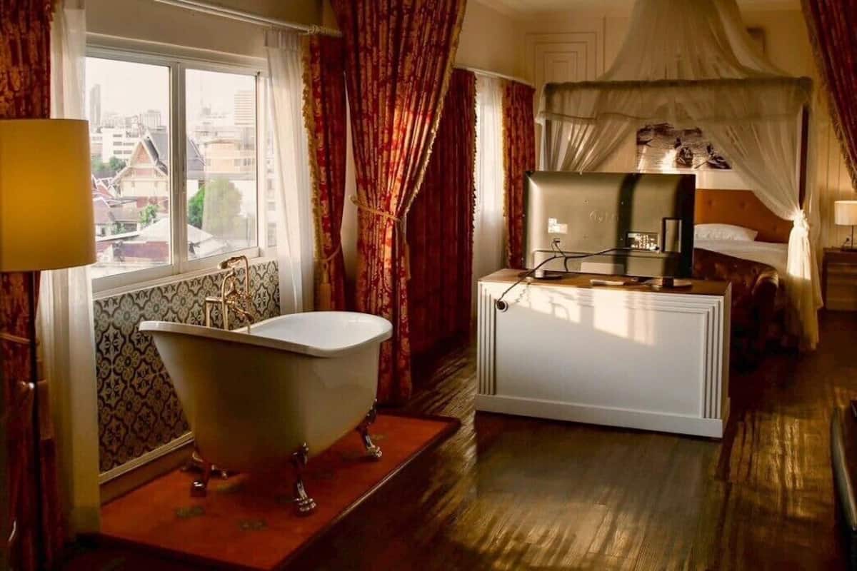A room with a bathtub, a bed with a canopy, and a window with curtains.
