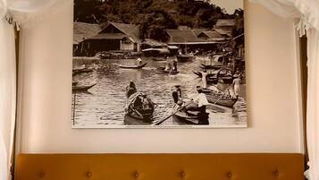 Ein Bett mit Kopfteil, ein an der Wand hängendes Bild von einem Marktplatz und ein Baldachin über dem Bett.