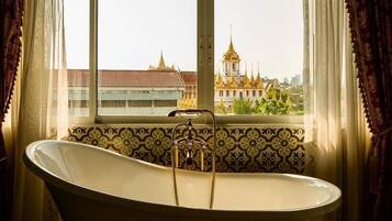 Une salle de bain avec une baignoire sur pieds, une fenêtre avec des rideaux et une vue sur un temple aux flèches dorées.