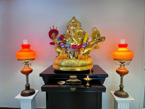 A golden statue of a deity with a trident, surrounded by flowers and incense burners, placed on a black pedestal with two ornate lamps on either side. - Siam Champs Elyseesi Unique Hotel (Bangkok)
