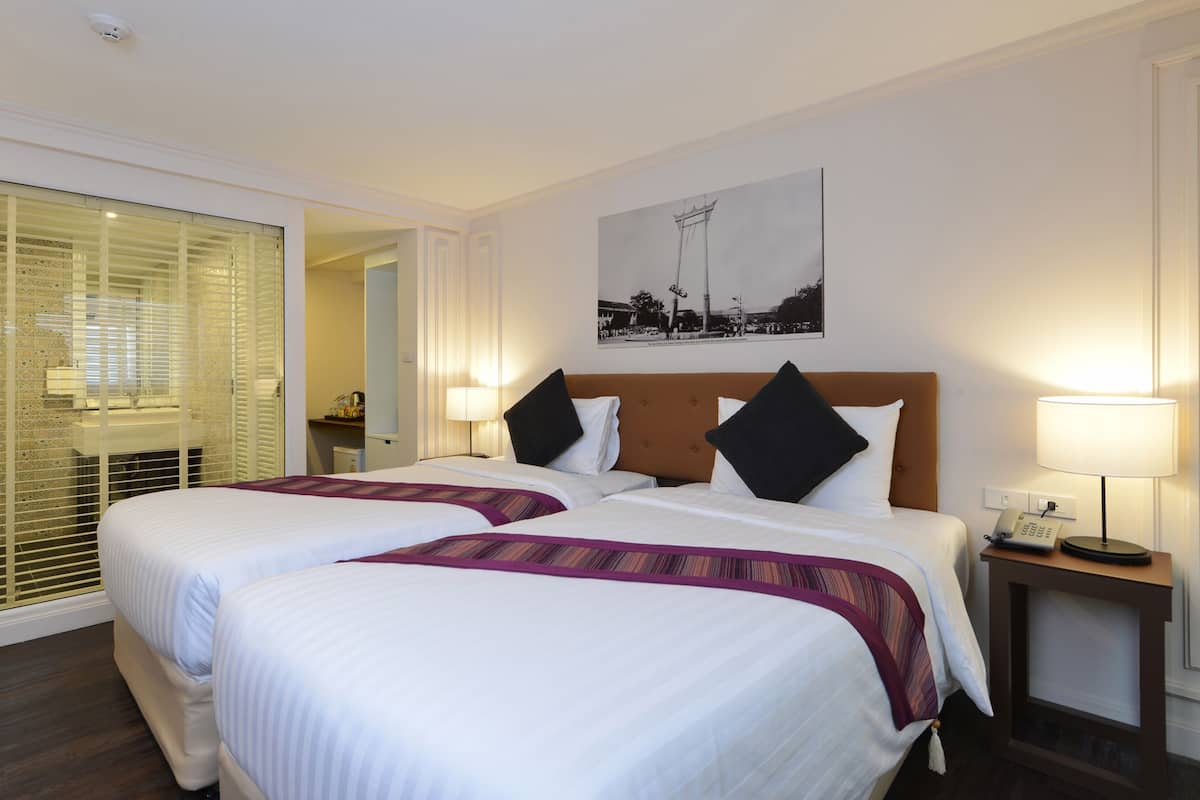 A hotel room with two beds, a bedside table with a lamp, a telephone, and a picture on the wall.