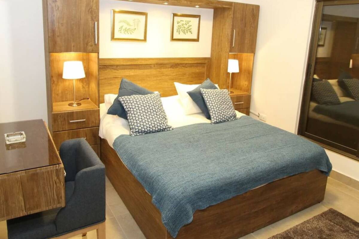 A bedroom with a wooden bed, two bedside tables with lamps, a small desk, and a large mirror.