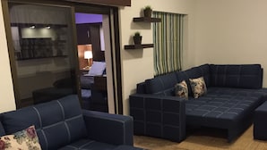 A living room with a sectional sofa, a round coffee table, and a view into another room through a glass door.