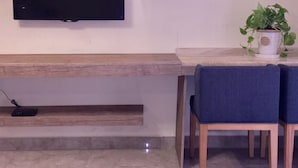 A modern living room with a flat-screen TV mounted on the wall, a wooden coffee table, two blue chairs, a small potted plant, and a built-in bench with a shelf below.