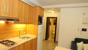 A compact kitchen with wooden cabinets, a gas stove, a sink, and a refrigerator.
