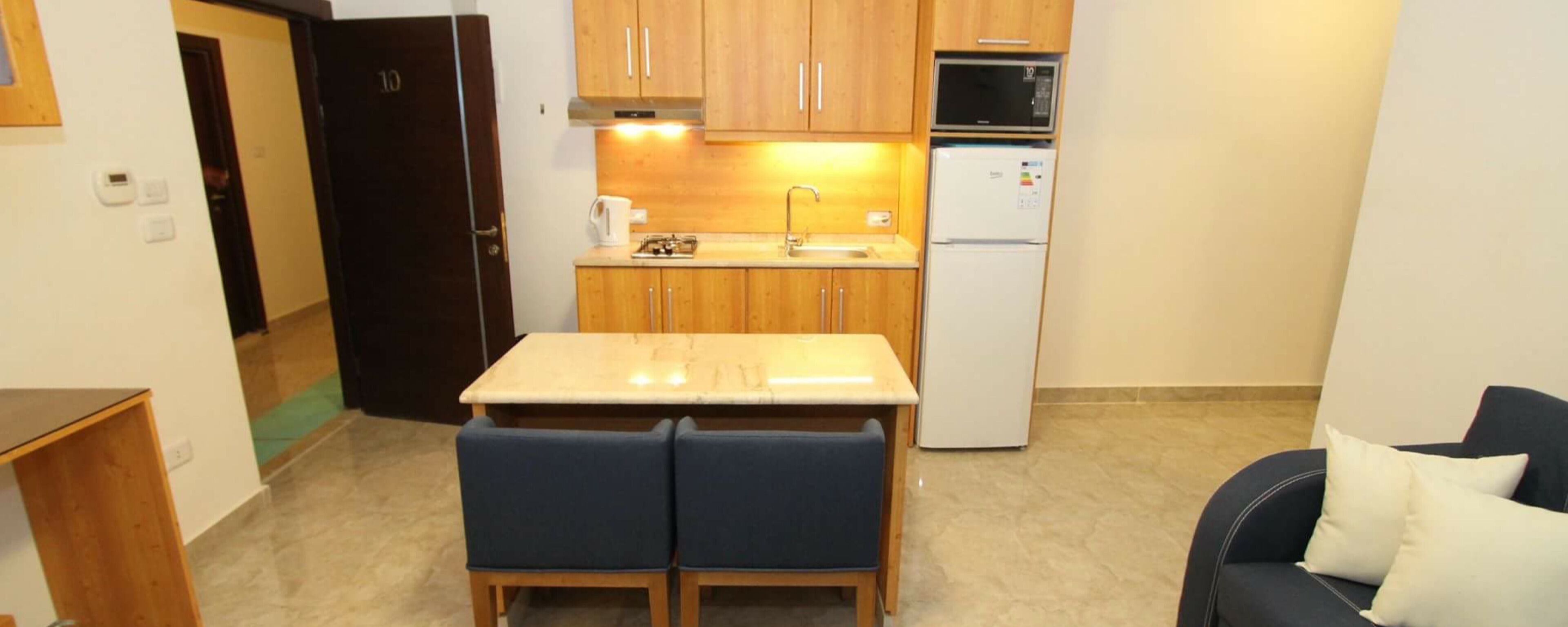 A compact kitchen with wooden cabinets, a microwave, and a refrigerator. There is a small dining table with two chairs.