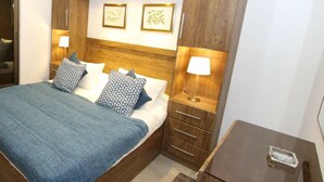 A hotel room with a large bed, wooden headboard, two bedside tables with lamps, a small wooden nightstand, and a mirror.