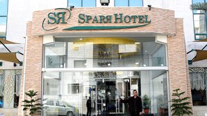 El exterior del Hotel Spar, con entrada de vidrio, plantas en macetas y un coche estacionado afuera.