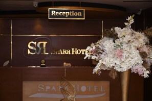 Een receptiebalie met een bord waarop 'Reception' en 'SIL SPA HOTEL' staan.