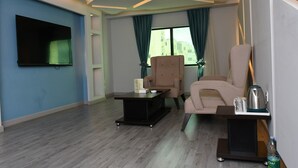 Una sala de estar moderna con un televisor de pantalla plana, dos sillones, una mesa de centro y una mesita auxiliar con una tetera y una botella de agua.