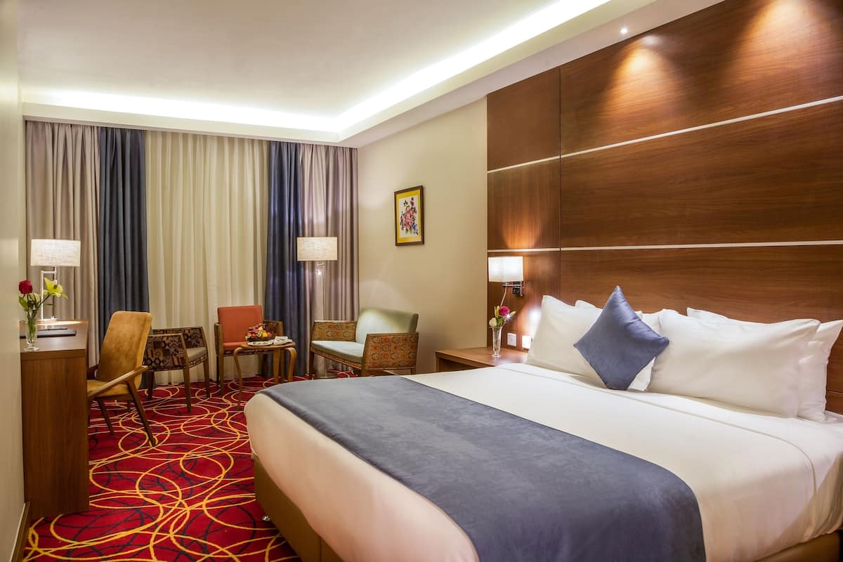 A hotel room with a large bed, two chairs, a desk, and a red carpeted floor.