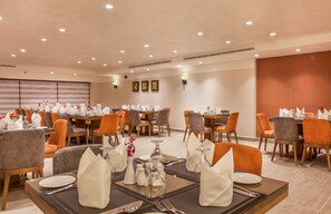 Un comedor de hotel con varias mesas dispuestas para los huéspedes, con vajilla y centros de mesa.