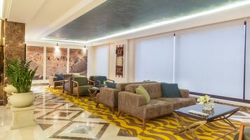 Un vestíbulo moderno con alfombra de diseño geométrico, un área de descanso con sofás y sillones, y un mural grande en la pared.
