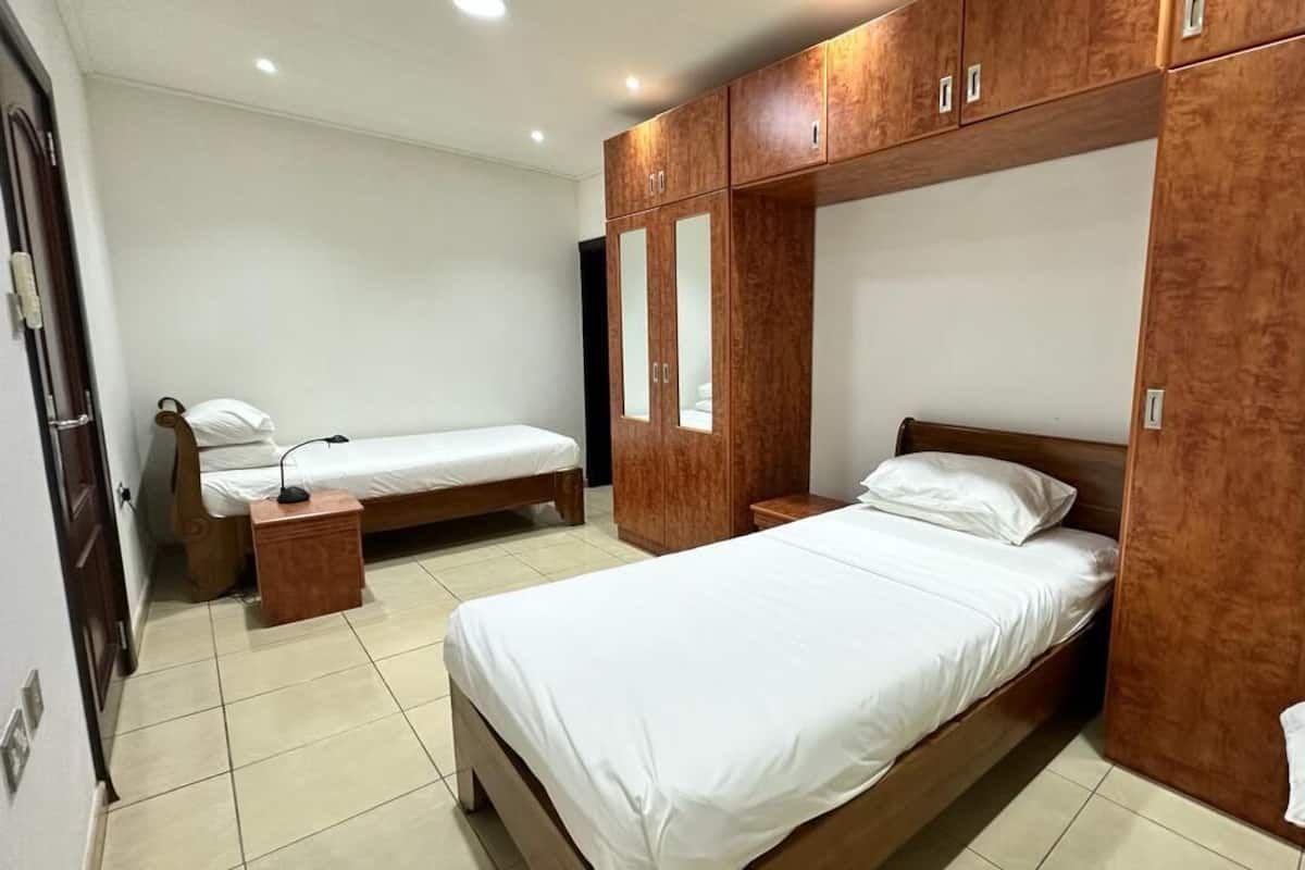 Un dormitorio con dos camas individuales, un armario de madera y una mesita de noche.