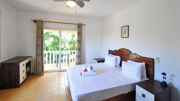 A hotel room with a bed, bedside table, and a ceiling fan. - GT Self Catering Apartments (Mahé Island)