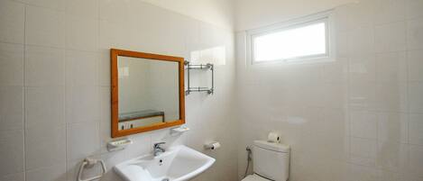 A small, clean bathroom with white tiles, a sink, a toilet, and a window providing natural light.