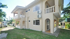 A two-story house with a balcony, a garage, and a well-maintained lawn. - GT Self Catering Apartments (Mahé Island)