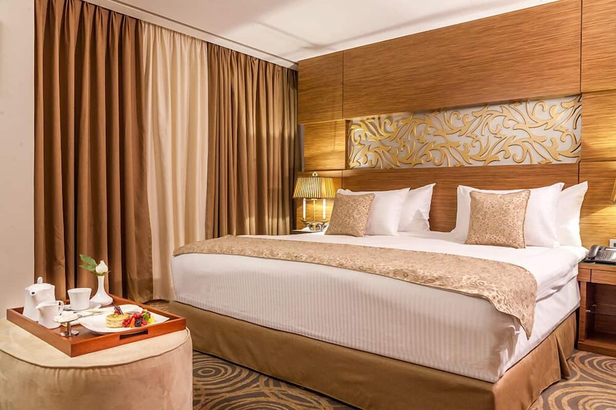 A hotel room with a large bed, a wooden headboard, a bedside table with a lamp, and a tray with breakfast items.