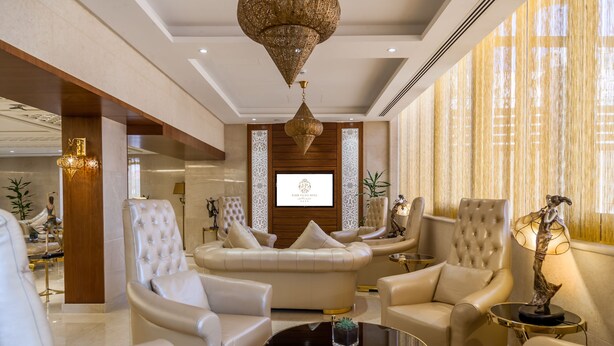 Un hall d’entrée luxueux, doté de sièges confortables, d’un grand lustre et d’une pancarte d’accueil encadrée.