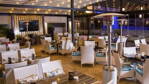 Un restaurant doté de meubles, de tables et de chaises en osier, d’une scène avec des instruments de musique et d’un grand écran.