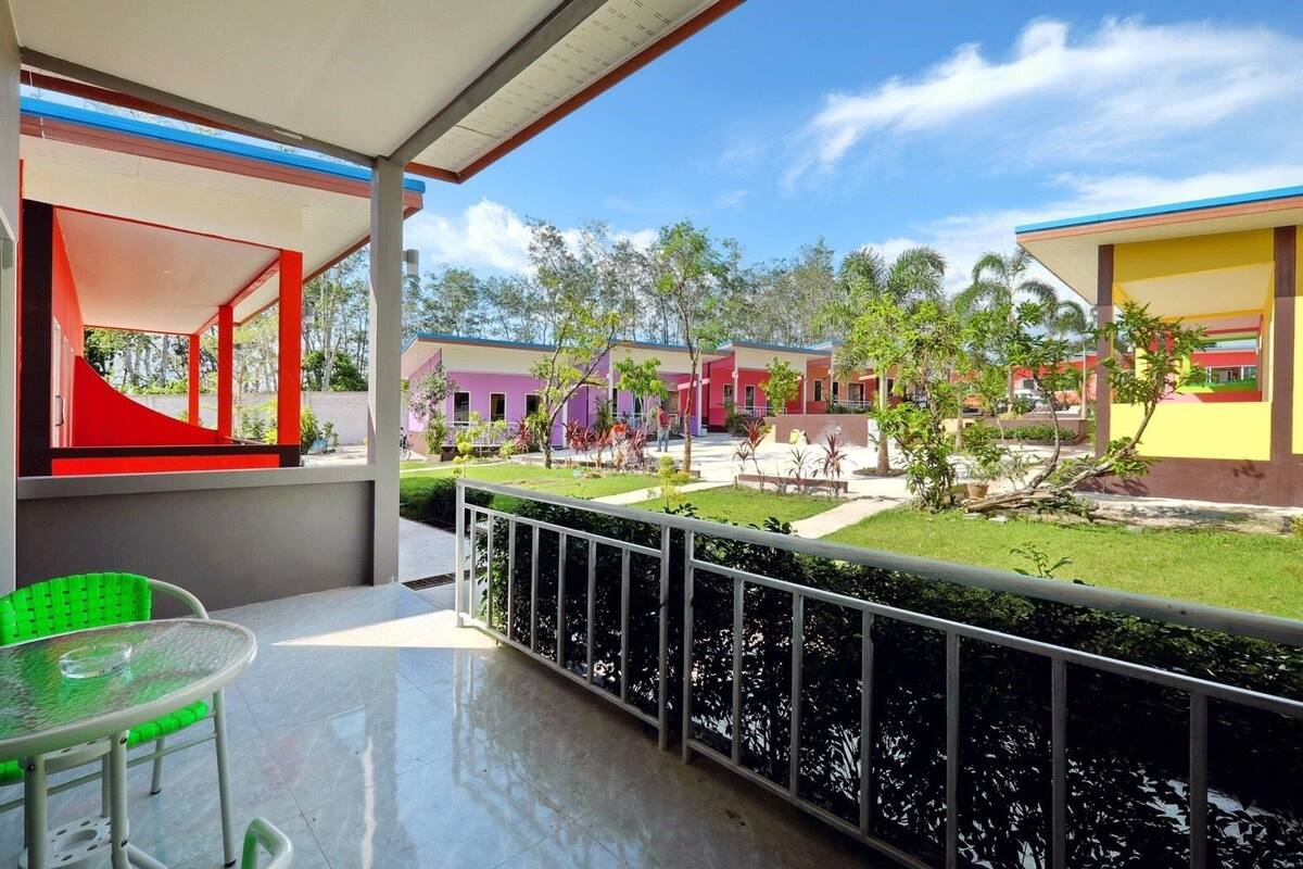 A covered outdoor area with a table and chairs, a view of colorful buildings, and a well-maintained lawn.