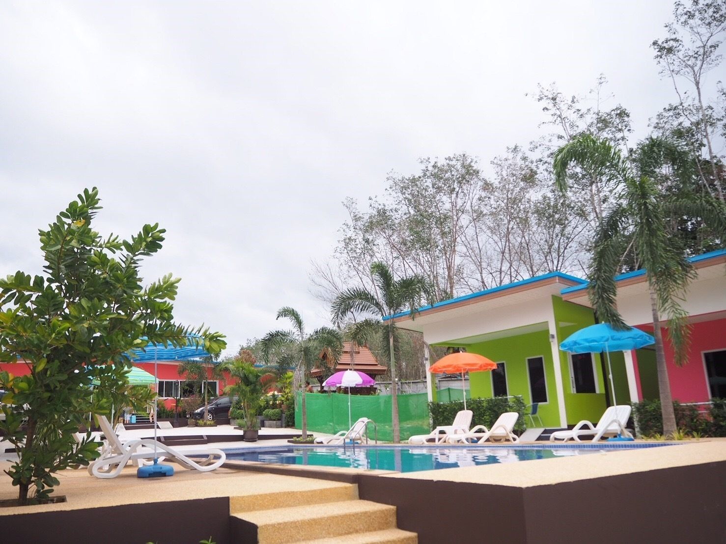 A pool area with lounge chairs and umbrellas, surrounded by greenery and buildings with colorful facades.