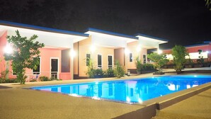 Ein Hotel mit Schwimmbad, mehreren Zimmern mit Balkonen und einer gut beleuchteten Außenfassade bei Nacht.