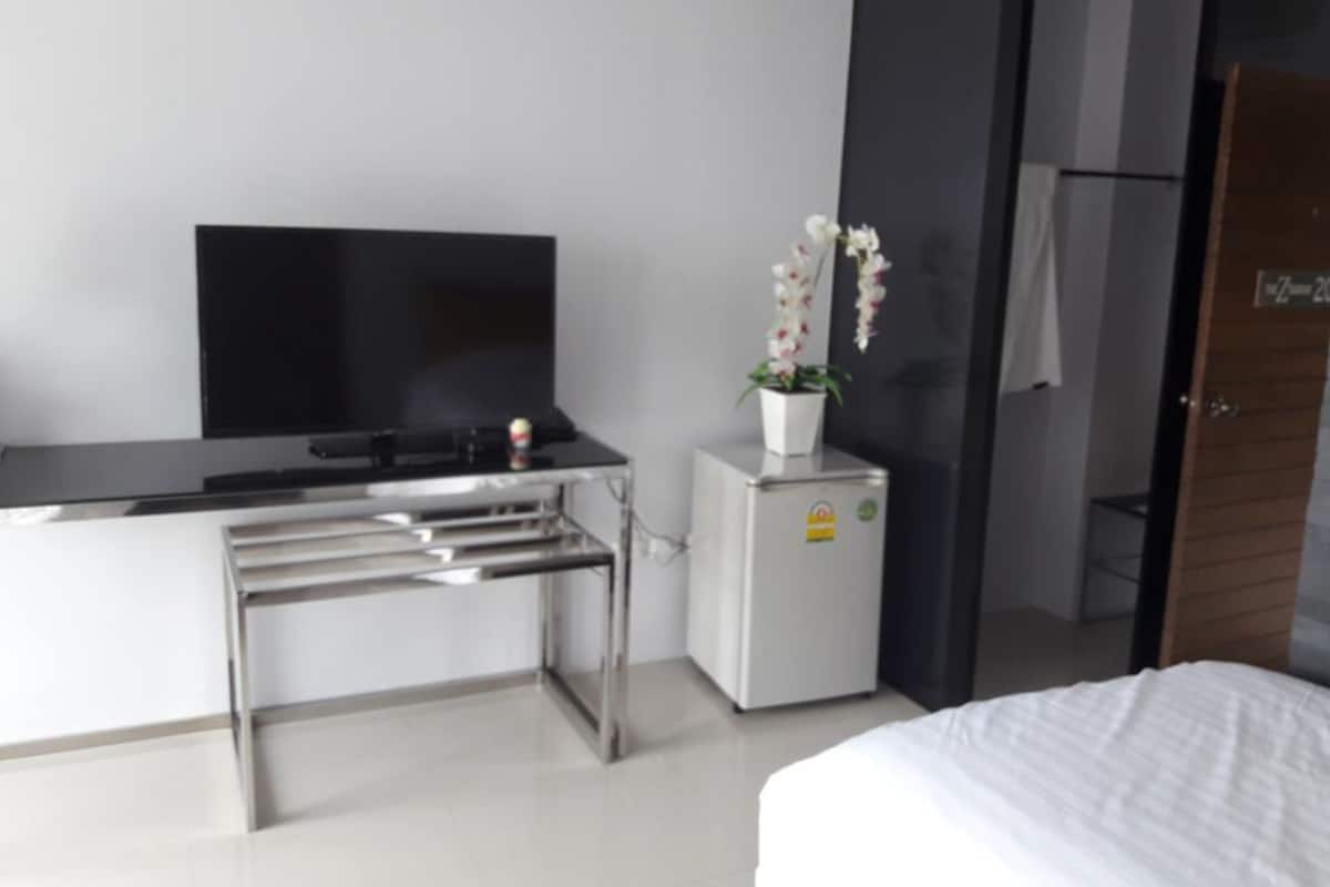 Een moderne hotelkamer met een bed, een klein bureau met een flatscreen televisie, een koelkast en een potorkidee.