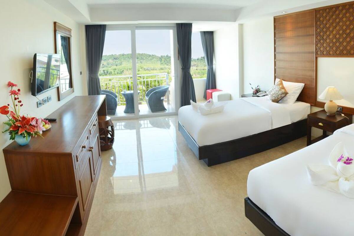 A hotel room with two beds, a TV, a desk, and a balcony with a view.