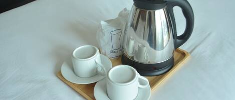 A tray with two white cups and a silver electric kettle on a white table.