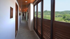 A corridor with large windows and wooden shutters, leading to a room with a view of a forested landscape. - David Residence (Mai Khao)