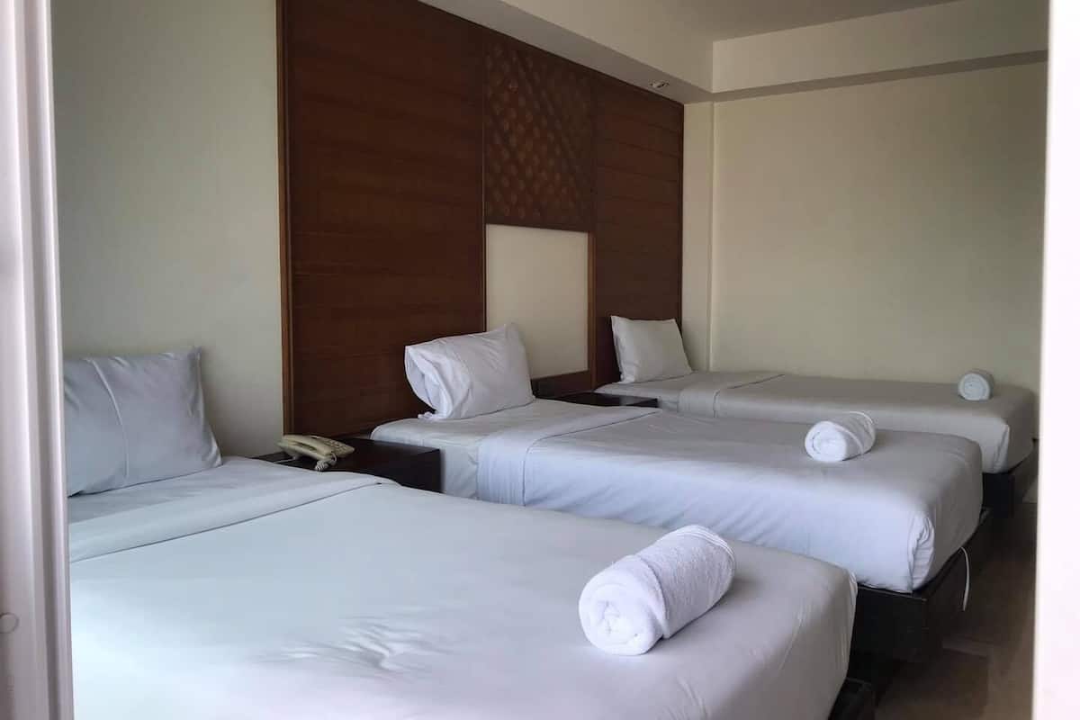 A hotel room with three single beds, each with a white pillow and a rolled towel.