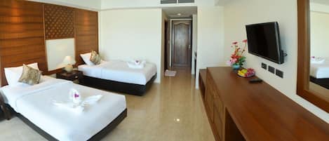 A hotel room with two beds, a TV, a wooden headboard, and a desk with a vase of flowers.