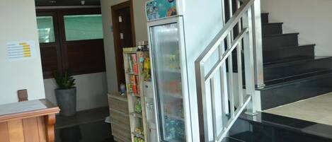 A hotel lobby with a refrigerator stocked with beverages, a staircase, and a reception desk.