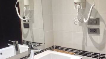 A bathroom with a white sink, a mirror, and a hairdryer mounted on the wall.