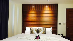 A hotel room with a large bed, wooden headboard, and a heart-shaped towel arrangement on the bed. - David Residence (Mai Khao)