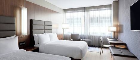 A hotel room with two beds, a desk, a chair, and a TV.